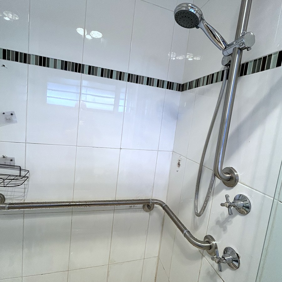 Angled stainless steel grab rail fixed in a tiled shower recess