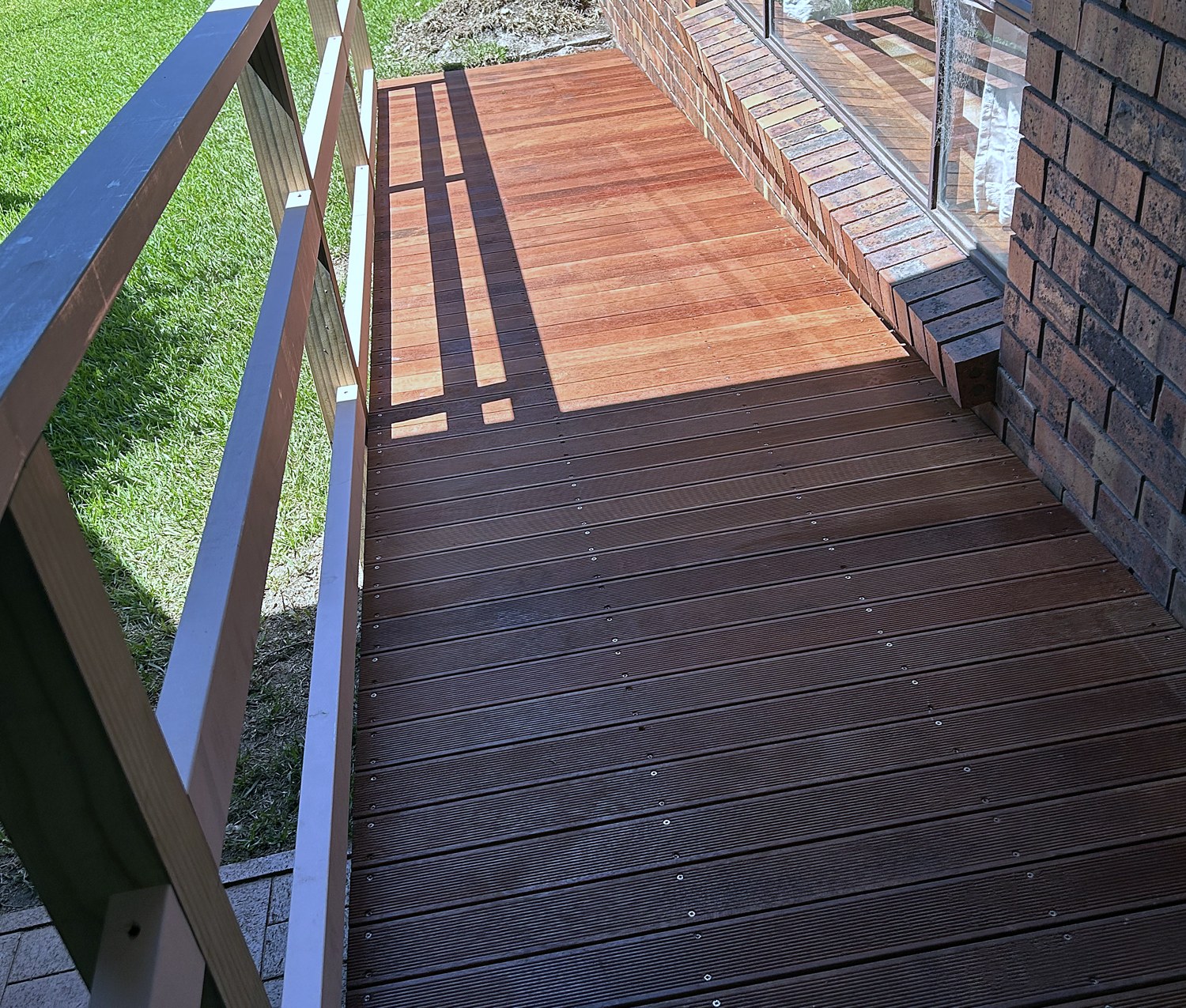 Timber wheelchair access ramp with handrails beside a brick home
